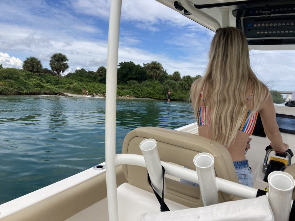 A blonde woman driving a boat on blue water, experiencing her Fall boating to-do list
